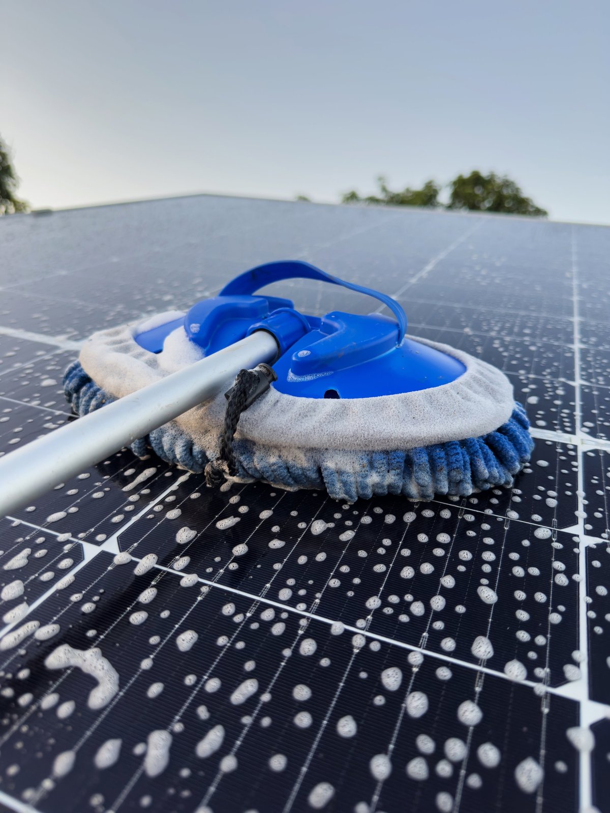 Professionelle Reinigung von Solarmodulen auf einem Dach – Schaum und Wasser werden mit einer Bürste aufgetragen